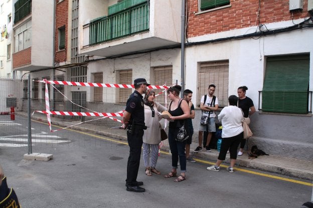 Varios vecinos que han desalojado sus pisos en el grupo Antonio Catalá y propietarias esperan en la calle junto a un agente de la Policía Local.