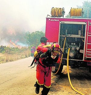 Ni un respiro. Dos efectivos de la Unidad Militar de Emergencias trabajan en la extinción del incendio iniciado en Cortes de Pallás. Al fondo de la imagen se observan las llamas del frente. ::
UME/