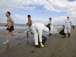 Bañistas corren por la playa, mientras técnicos de limpieza recogen muestras de fuel de la orilla de la playa./