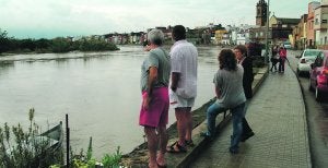 GRAN CAUDAL. Vecinos de Riola observan con preocupación el nivel del Júcar en la mañana de ayer. A media tarde la situación comenzó a mejorar. / JUAN PENADÉS/