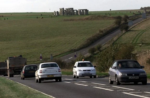 Los vehículos circulan por la carretera próxima a Stonehenge, que se recorta contra el horizonte. / ap
