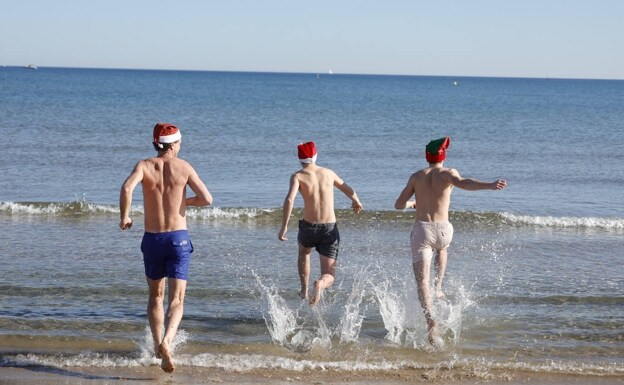Tres jóvenes se bañan en la playa del Cabanyal el día de Navidad con gorros de Papá Noel. 